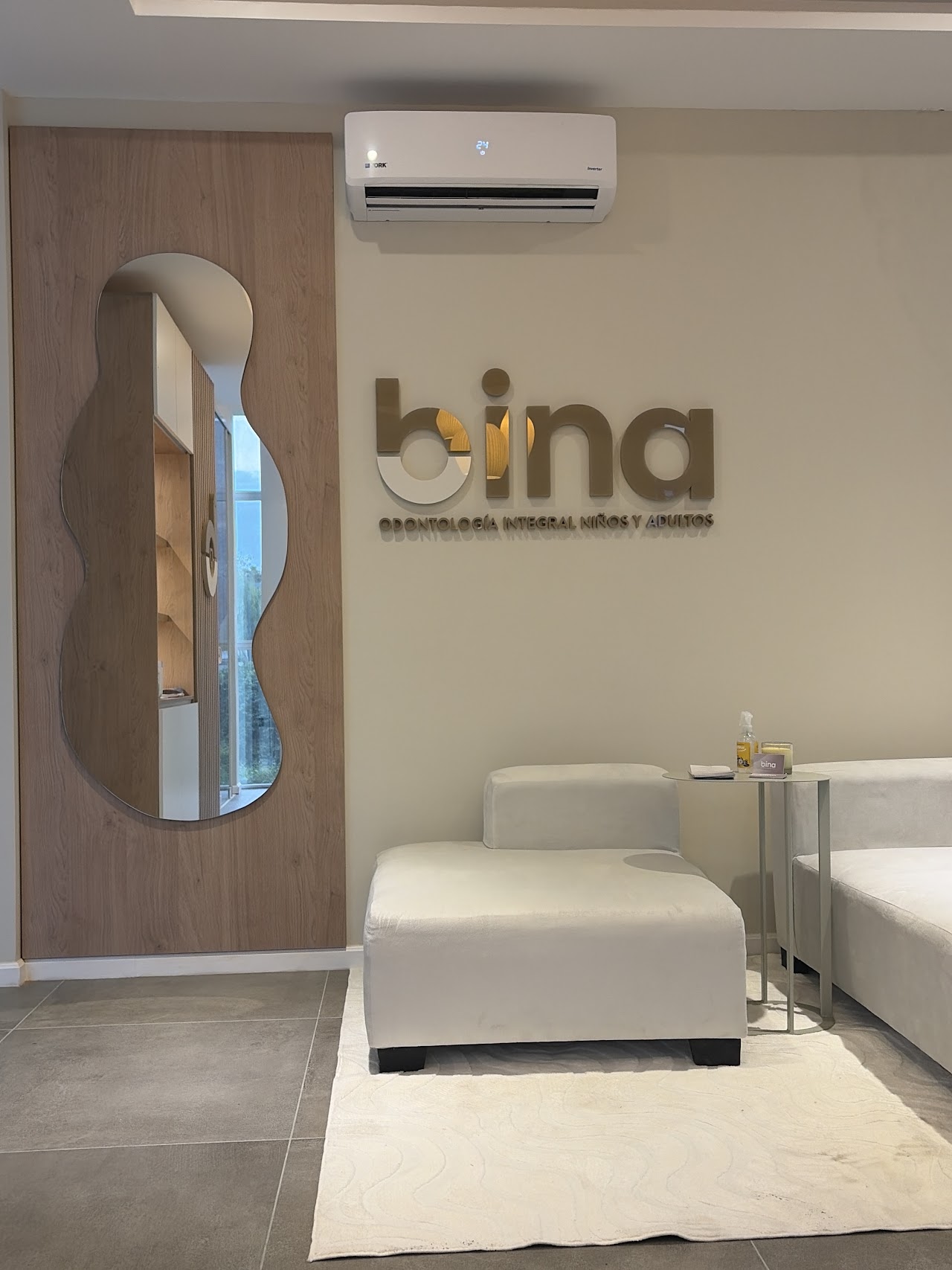 Recepción boutique con mostrador de roble acanalado y sillones boucle en BINA Odontología